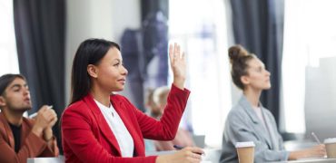 Side view portrait of smiling mixed-race businesswoman raising hand in class during training course on business and management, copy space